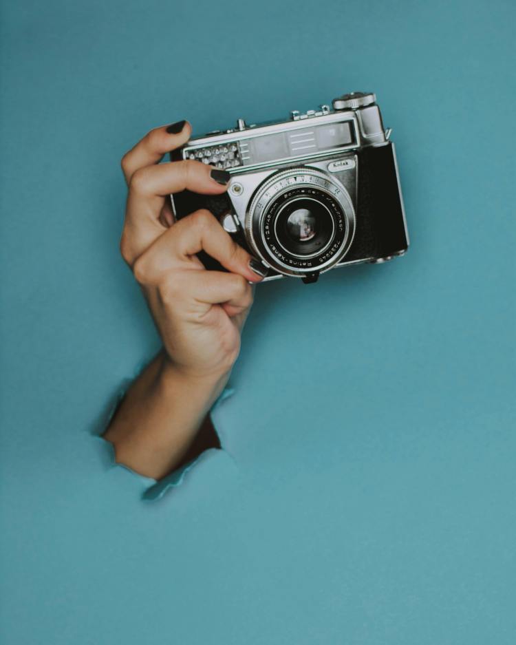 Image of hand coming through blue background holding a camera